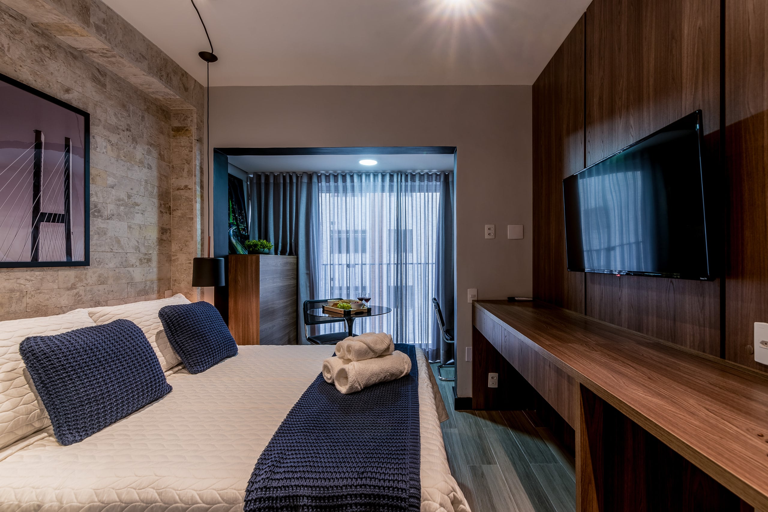 Cama de casal com roupa de cama azul-marinho e vista para a janela