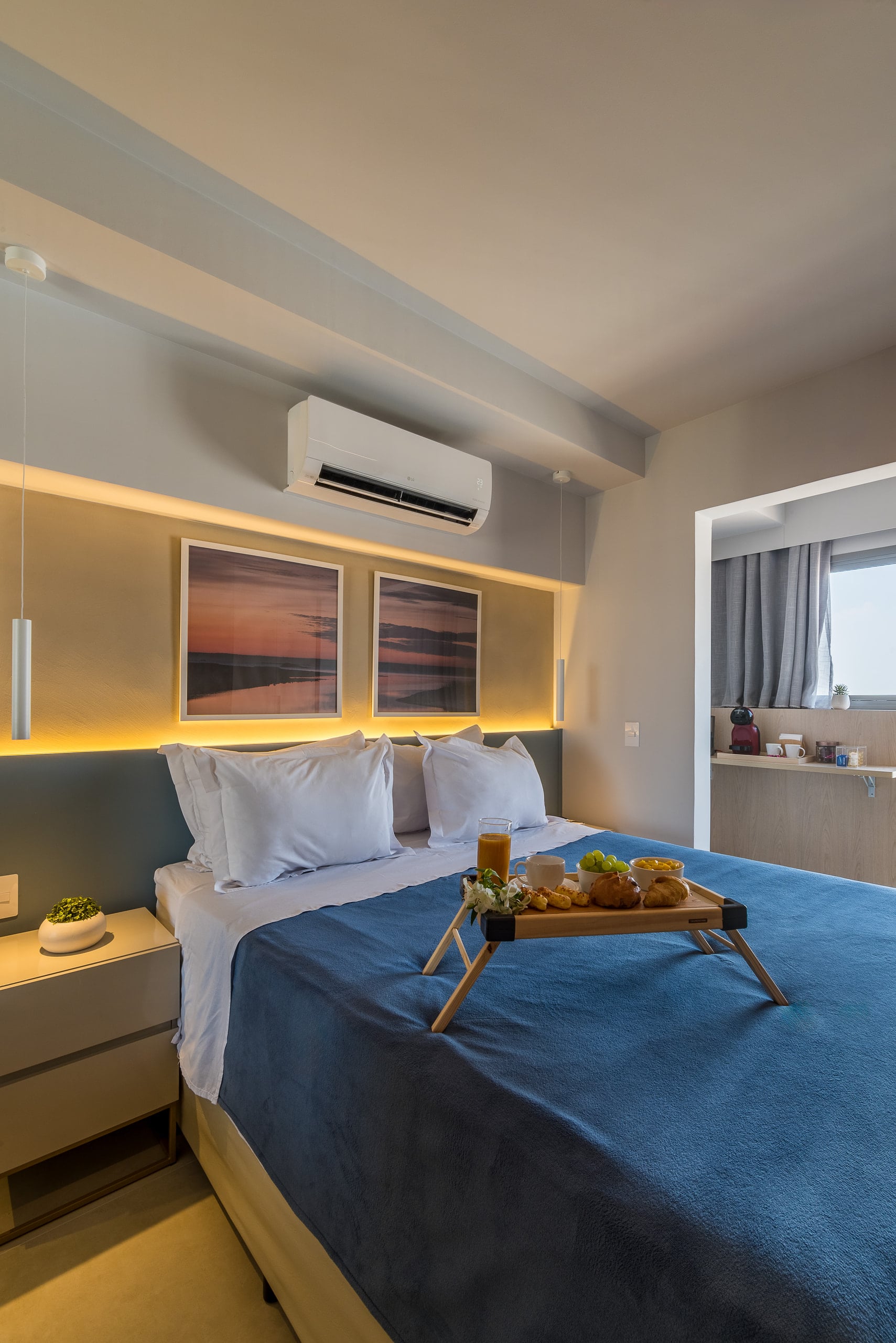 Cama de casal com cabeceira azul, arte na parede e bandeja de café da manhã