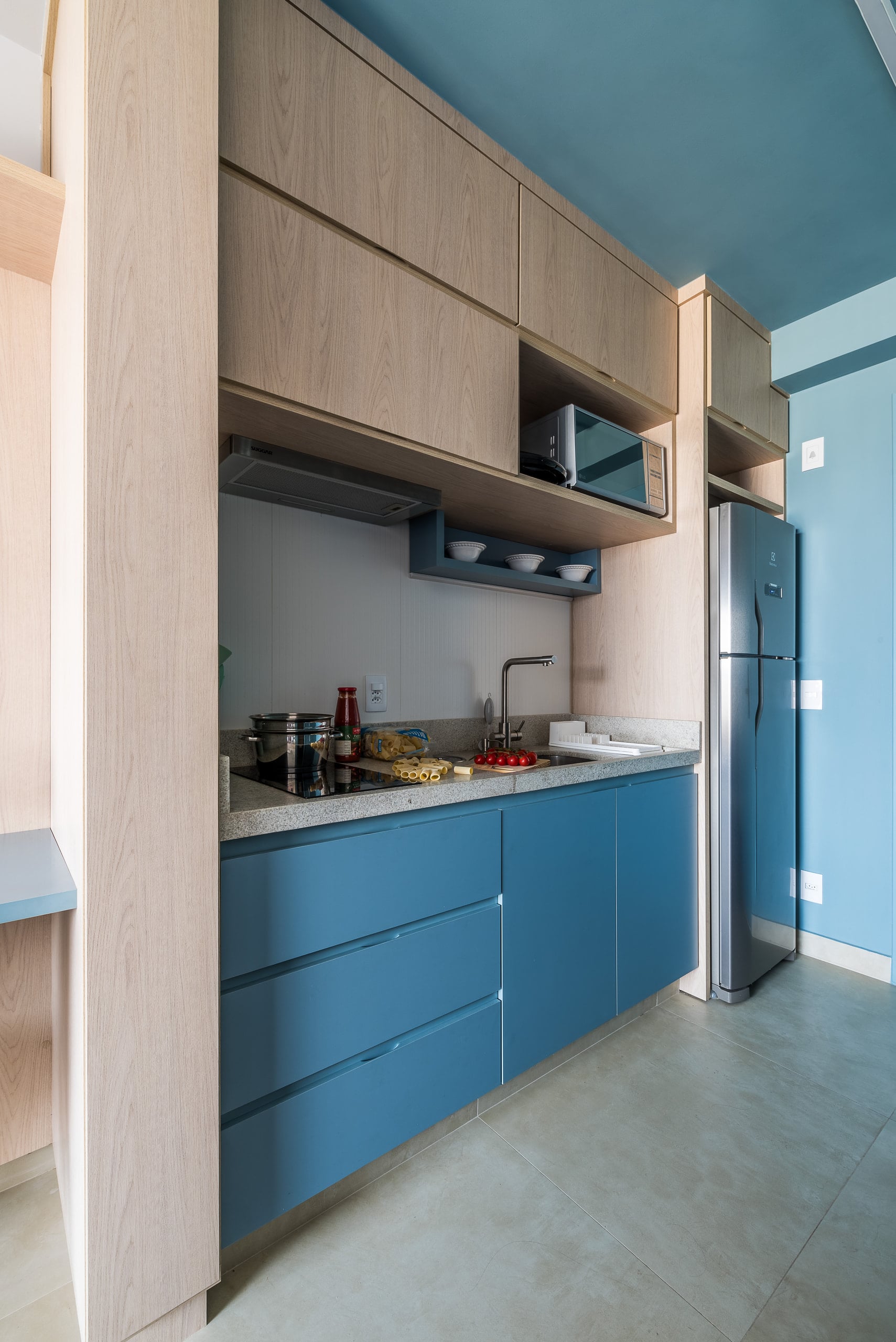 Cozinha compacta em marcenaria azul com bancada clara e geladeira embutida