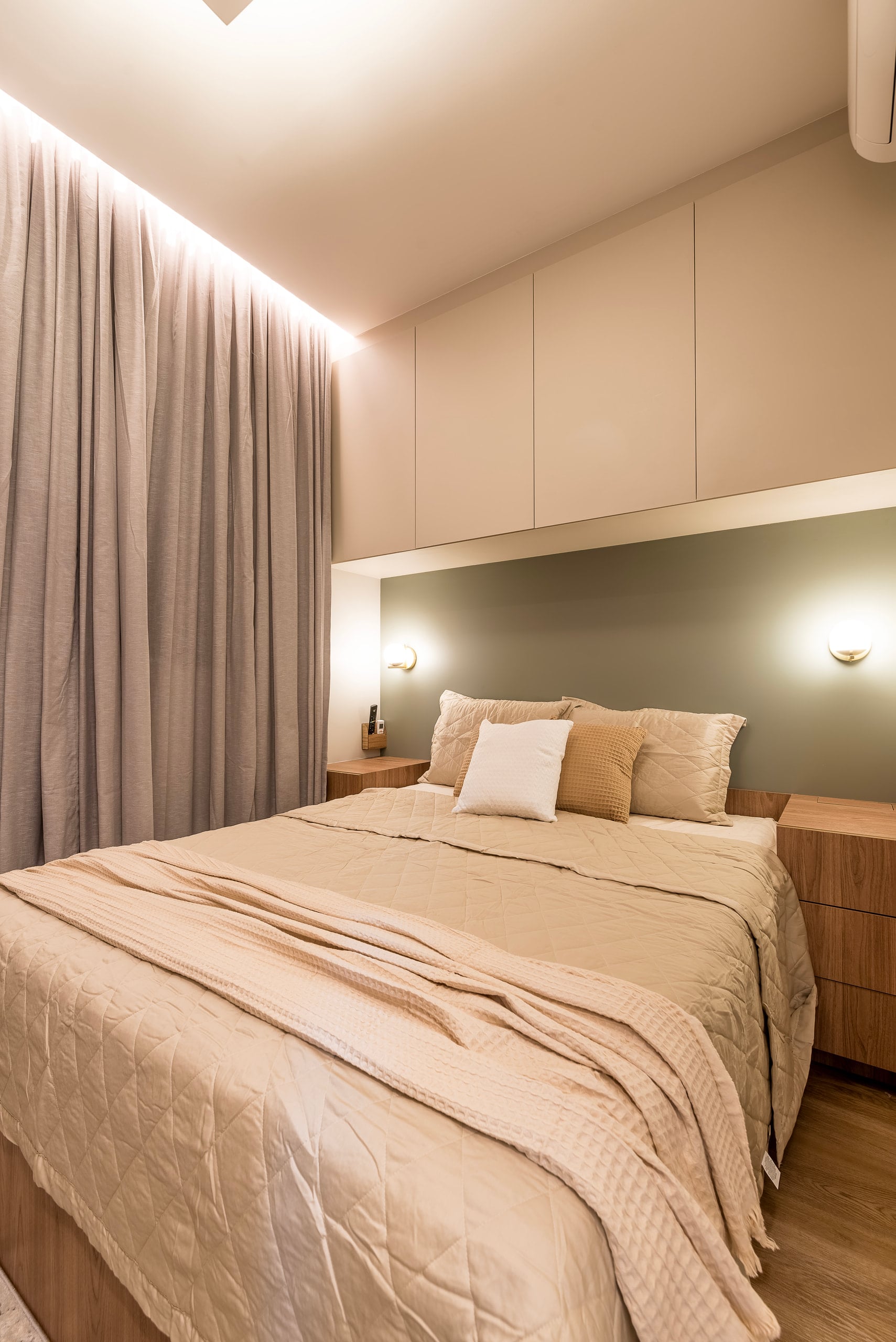 Cama da suíte vista de frente, com marcenaria clara e cortina de linho ao fundo