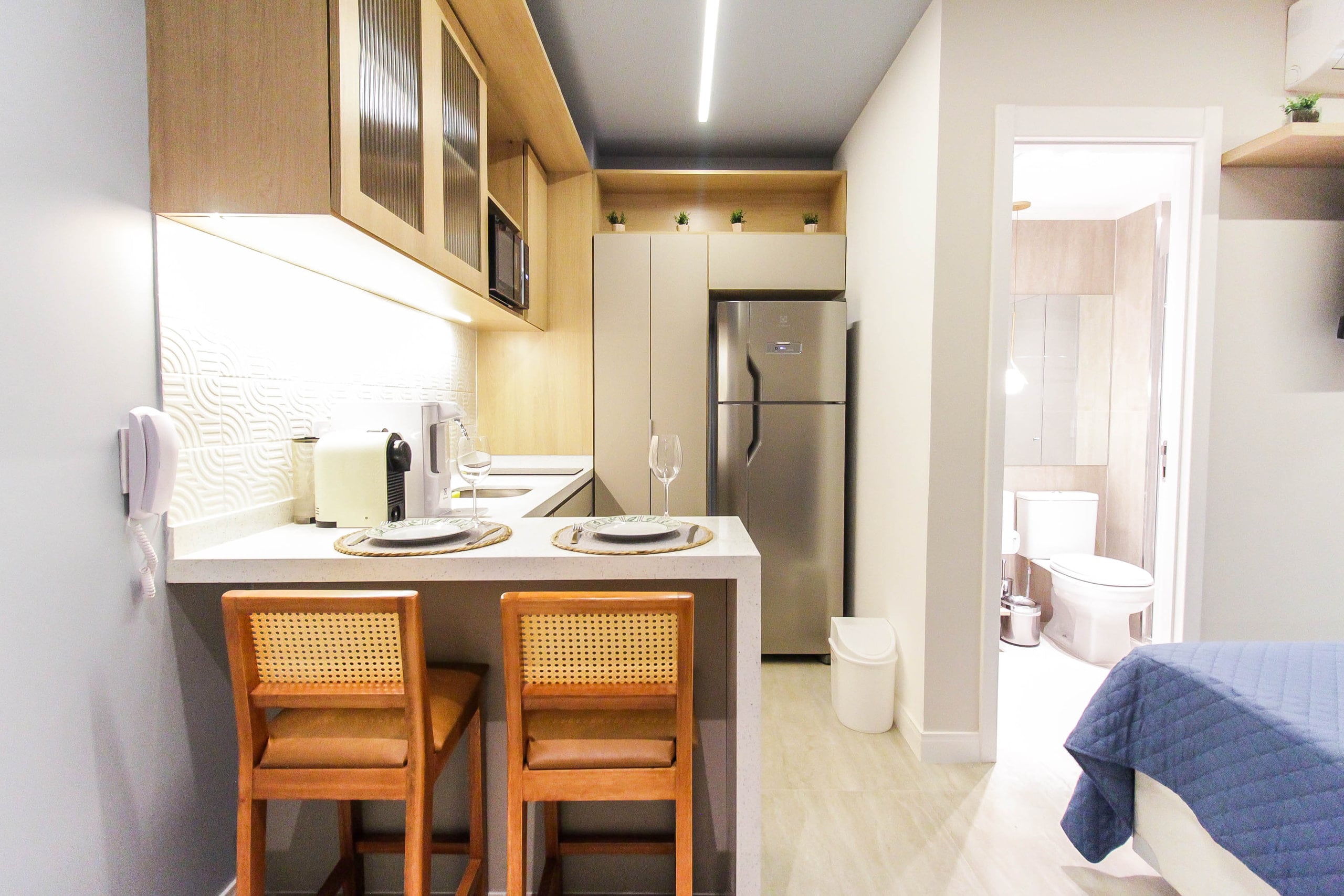 Cozinha compacta com cooktop, geladeira e armários claros até o teto