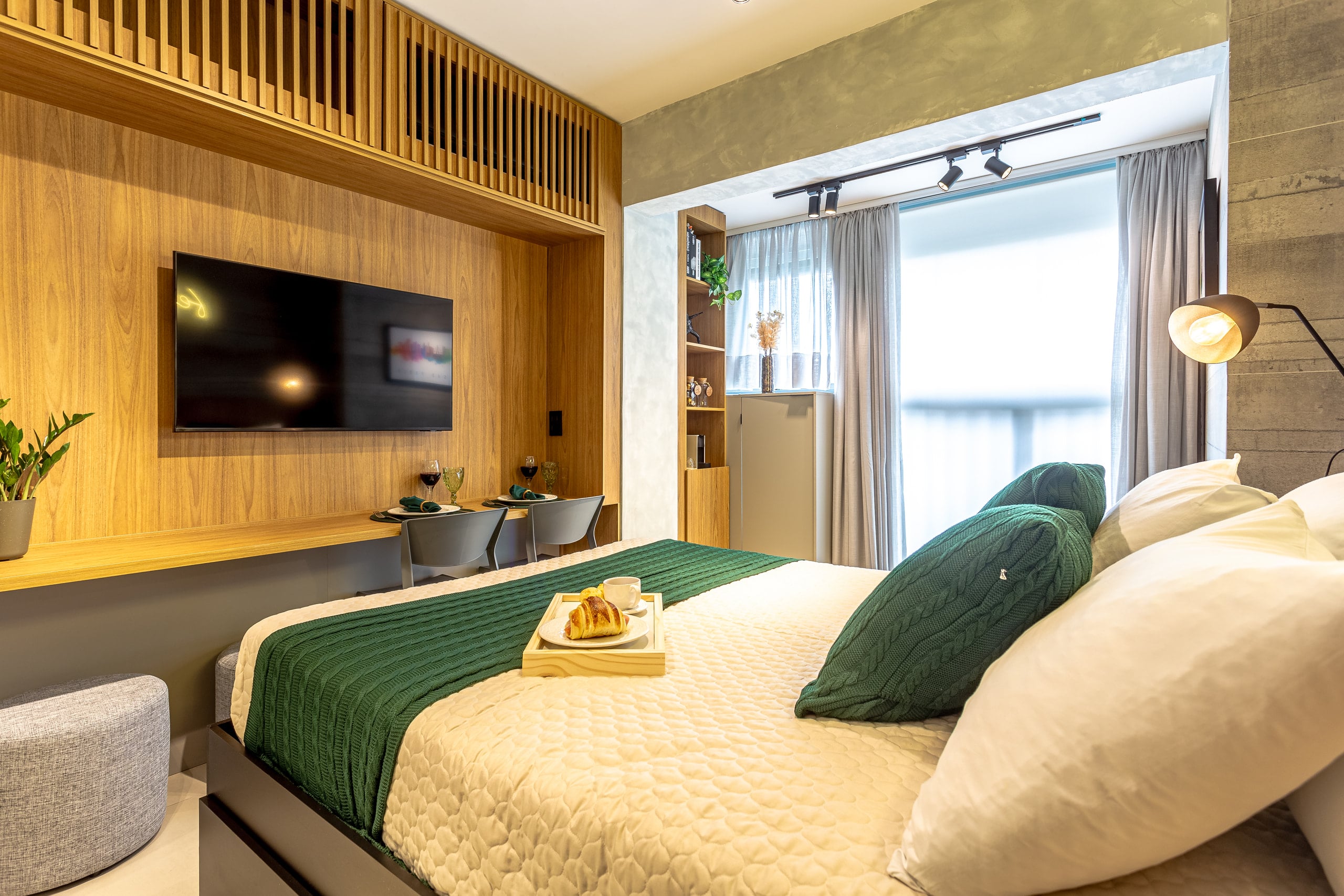 Cama de casal com enxoval verde e bandeja servida, sob o painel de madeira