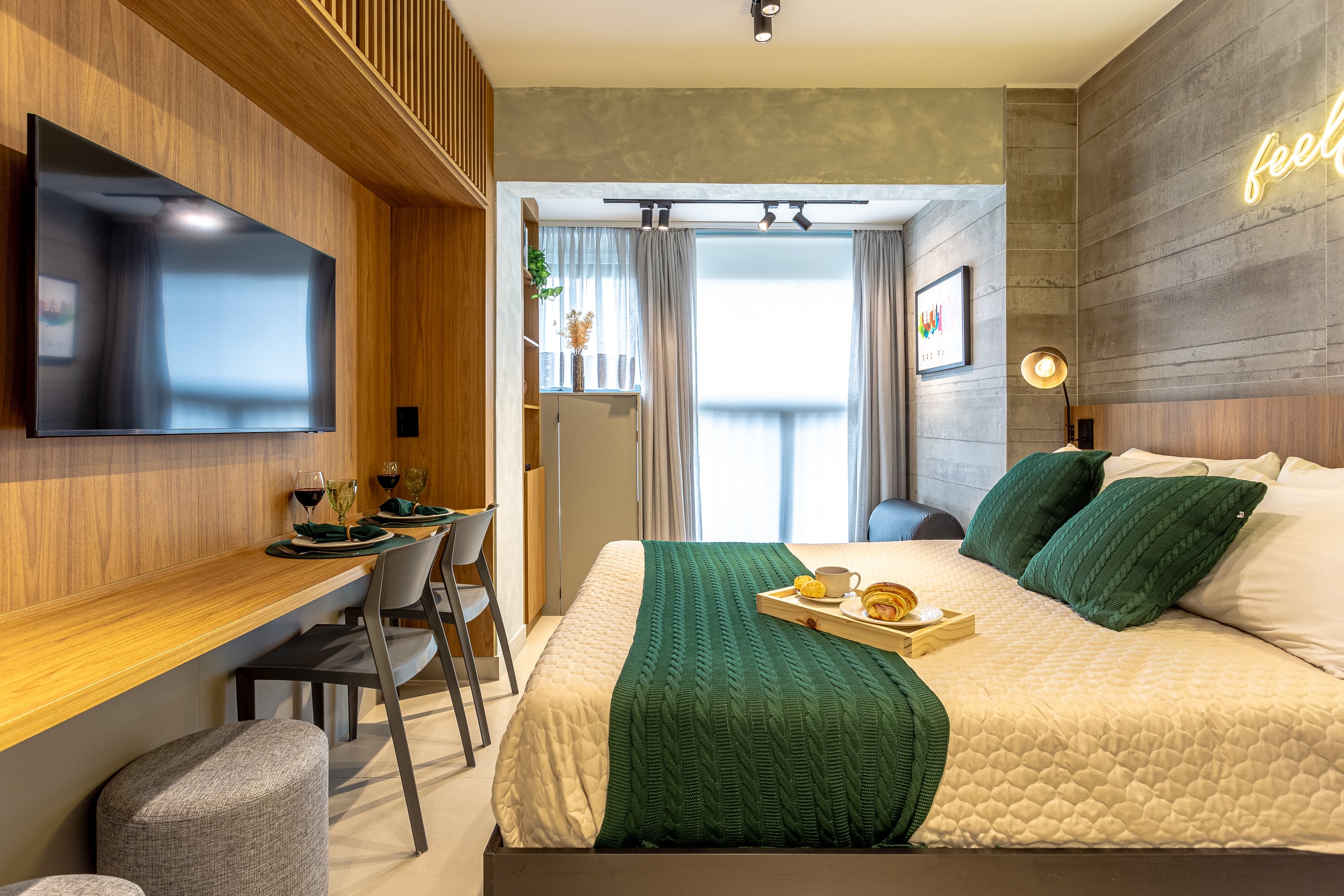 Bancada de refeições em primeiro plano e a cama ao fundo, junto à janela