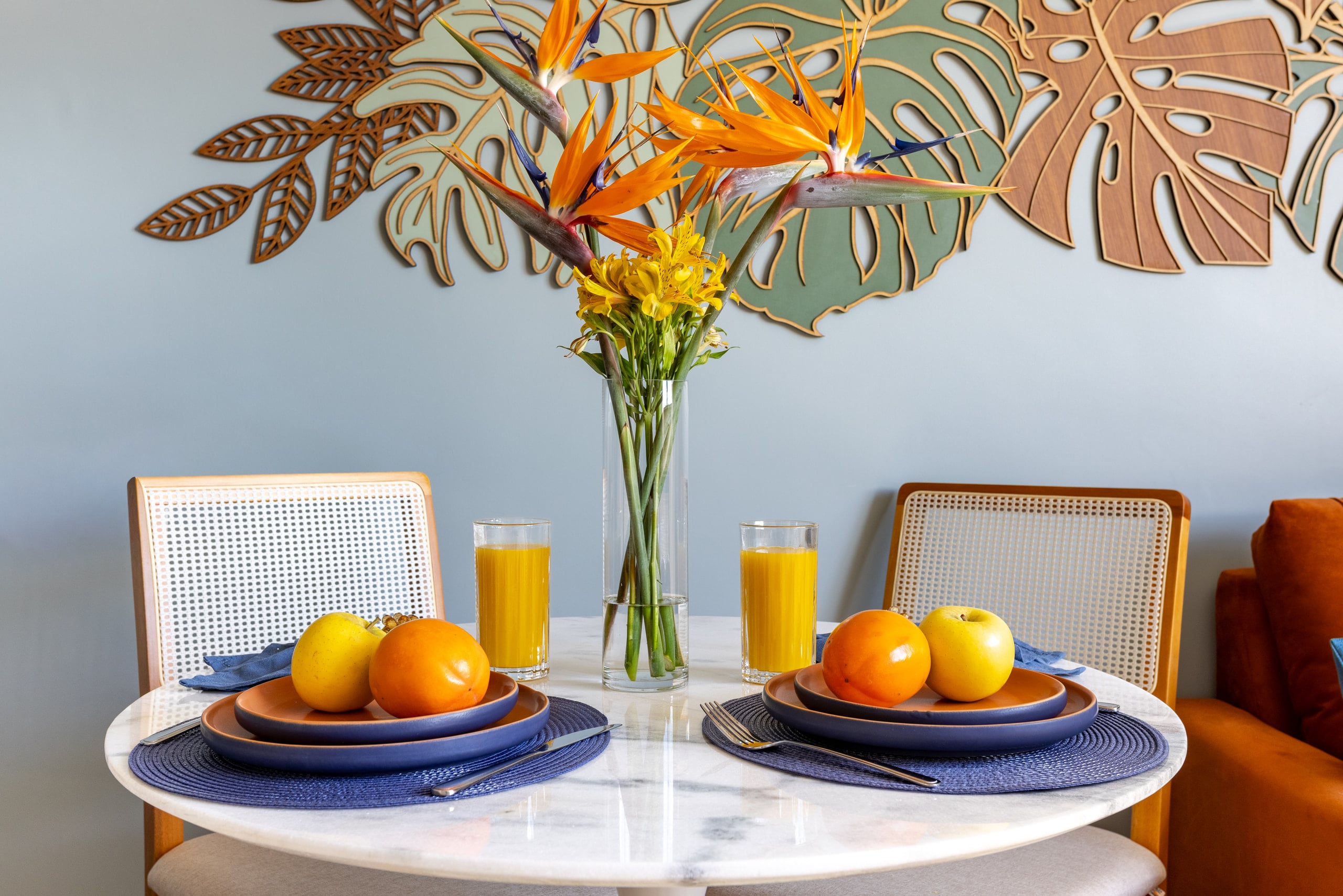 Mesa posta com frutas e suco diante do mural de folhagens