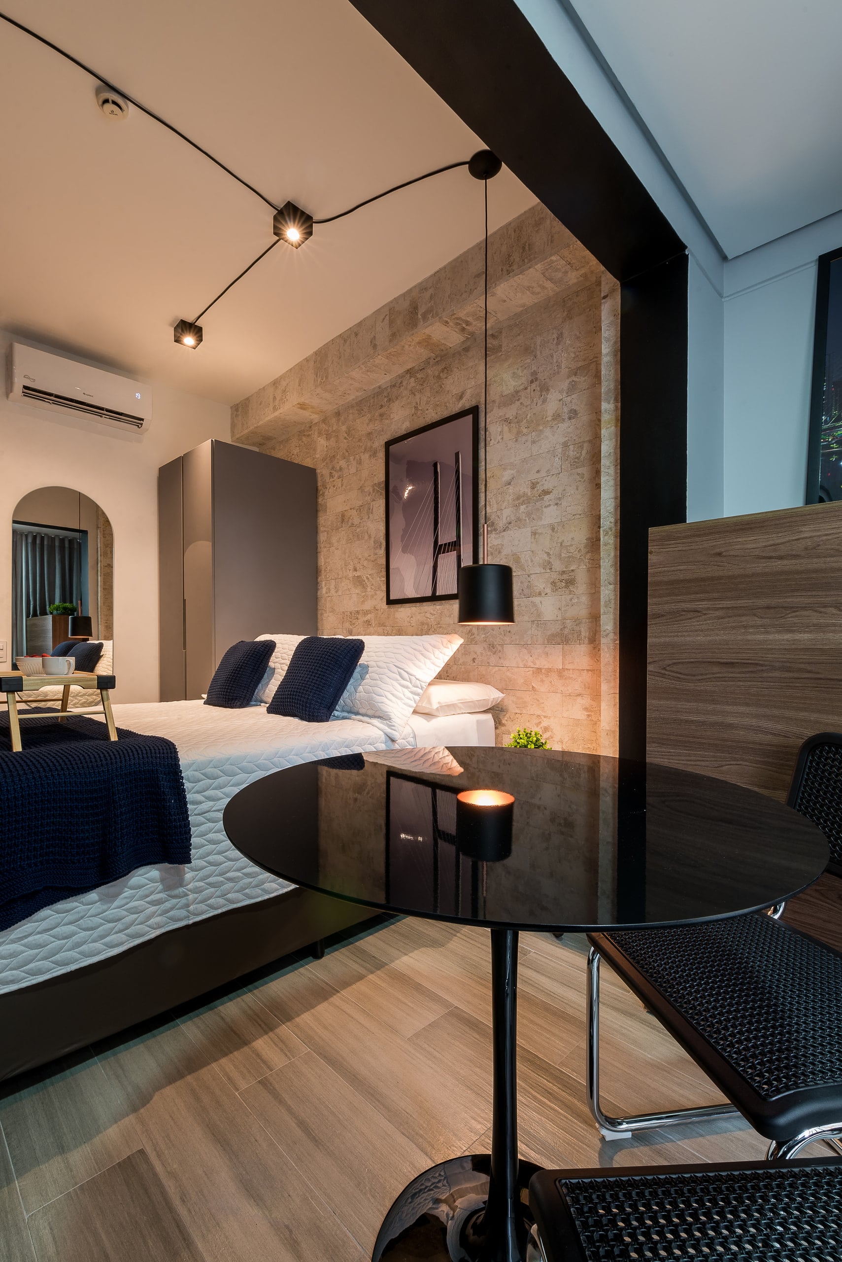 Studio com cama, mesa de refeições e painel de madeira integrando os ambientes