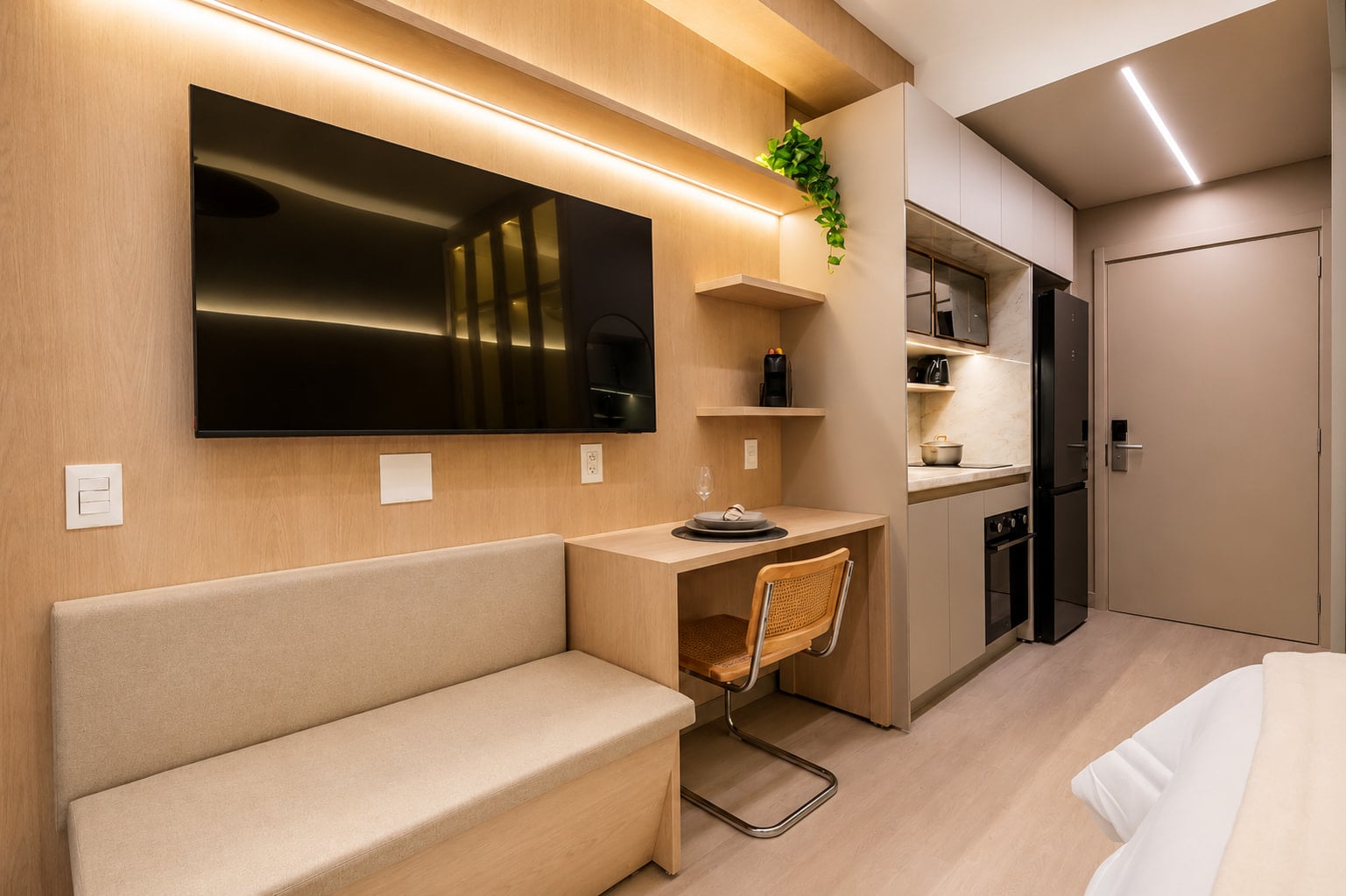Studio com bancada de trabalho, sofá e cozinha em marcenaria clara
